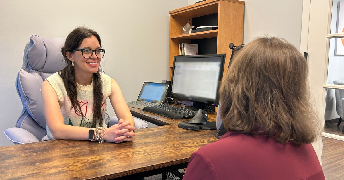 A Career Development Partners coach smiles during a one-on-one coaching session with a participant at her desk.